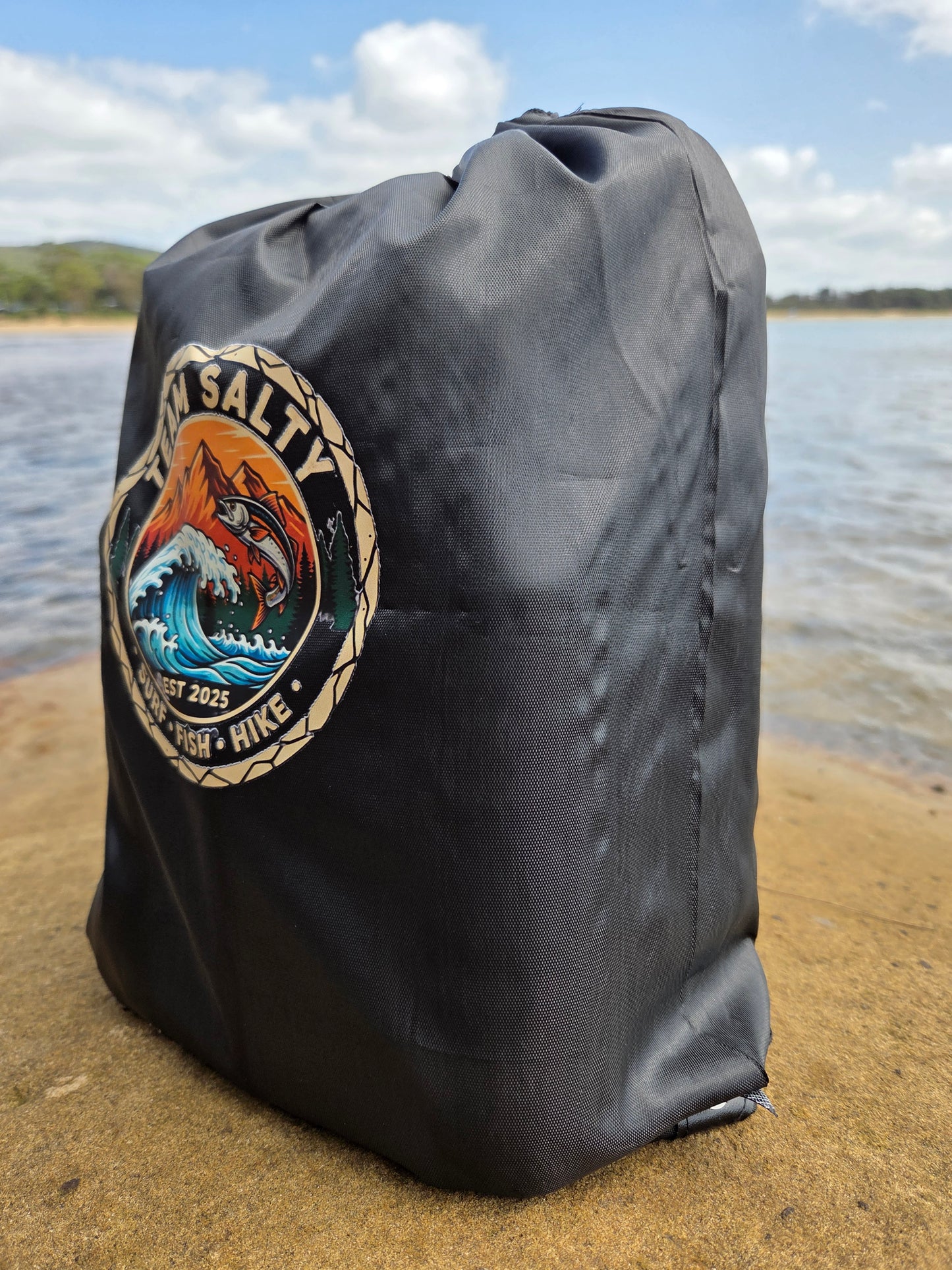Black bag with a logo on a sandy surface with water in the background